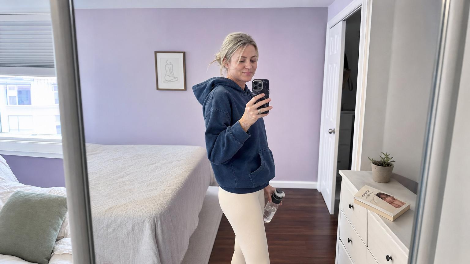 Different patient case (Caucasian woman in her late thirties) at day 14 after Korean multi-zone liposuction of the flanks and abdomen showing the high-compression body garment fitted over the trunk with subtle residual swelling visible at the lateral waistline, photographed in a soft pink and dusty gray Korean clinic follow-up room with a hand-written compression garment compliance schedule on the side table